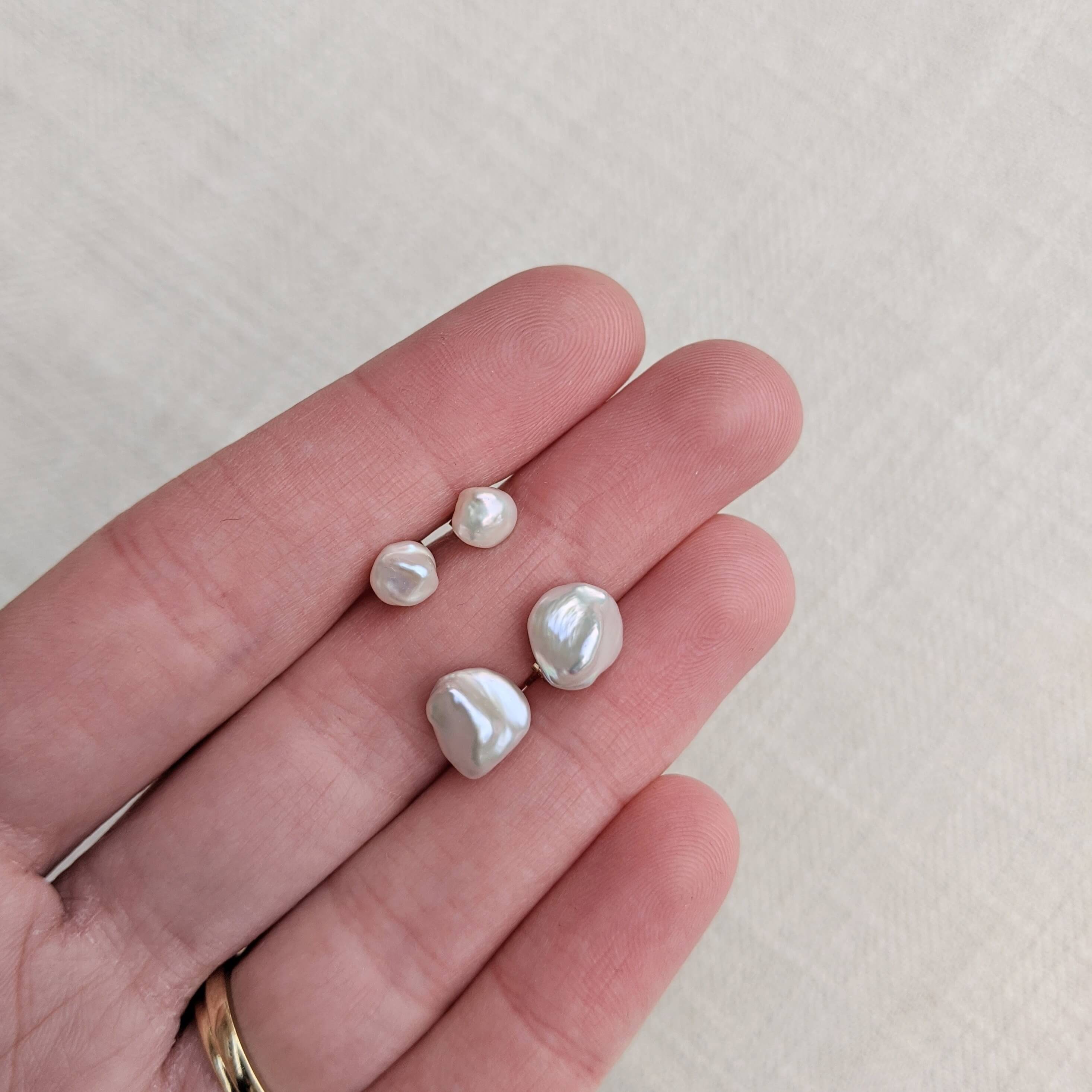 Hand holding different sized irregular pearl earrings